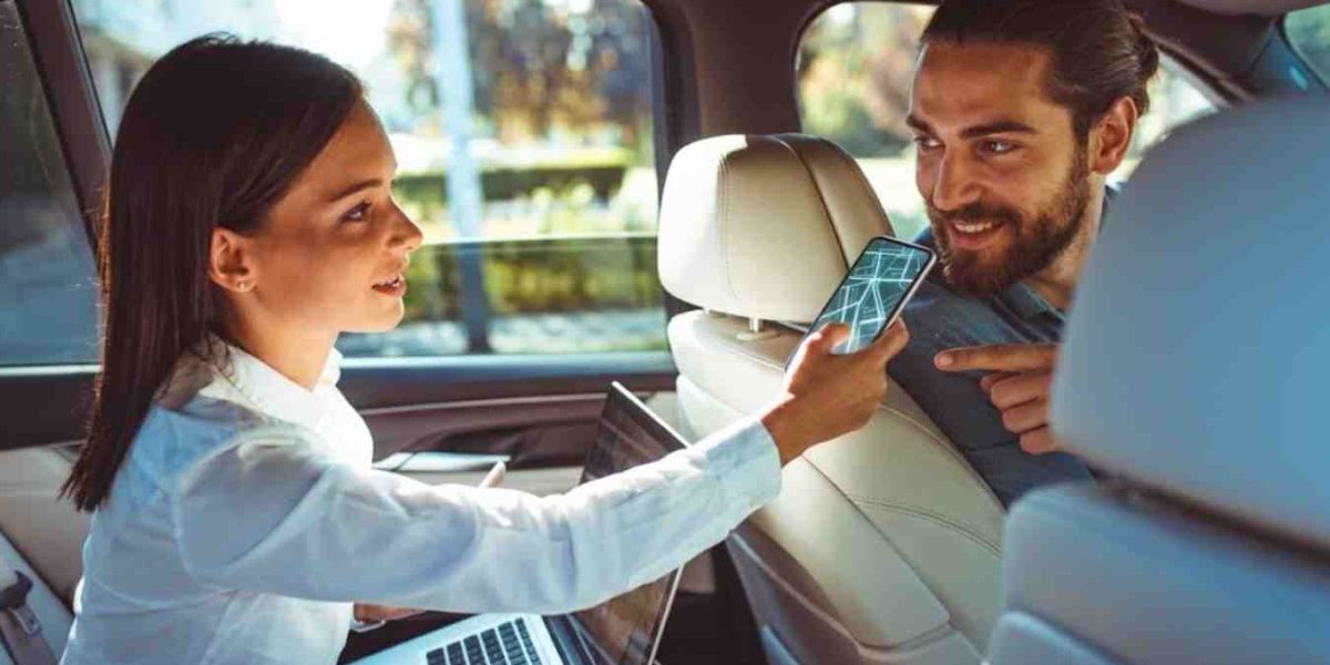 A taxi driver showing a passenger the route and location on a smartphone inside a cab.